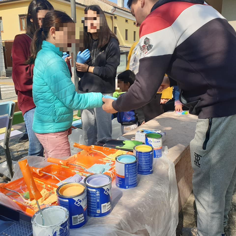 Volontari impegnati nella coloritura delle panchine con vasi dei cinque colori simbolici