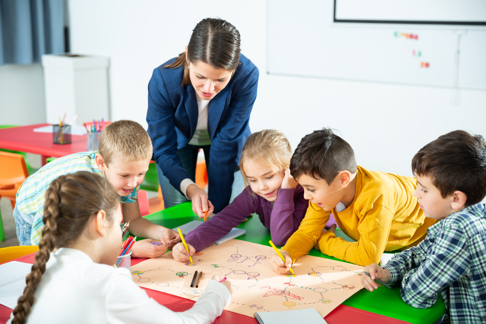 Bambini in gruppo seduti al banco che lavorano insieme guidati dall'insegnante che attiva una educazione precoce che previene il bullismo